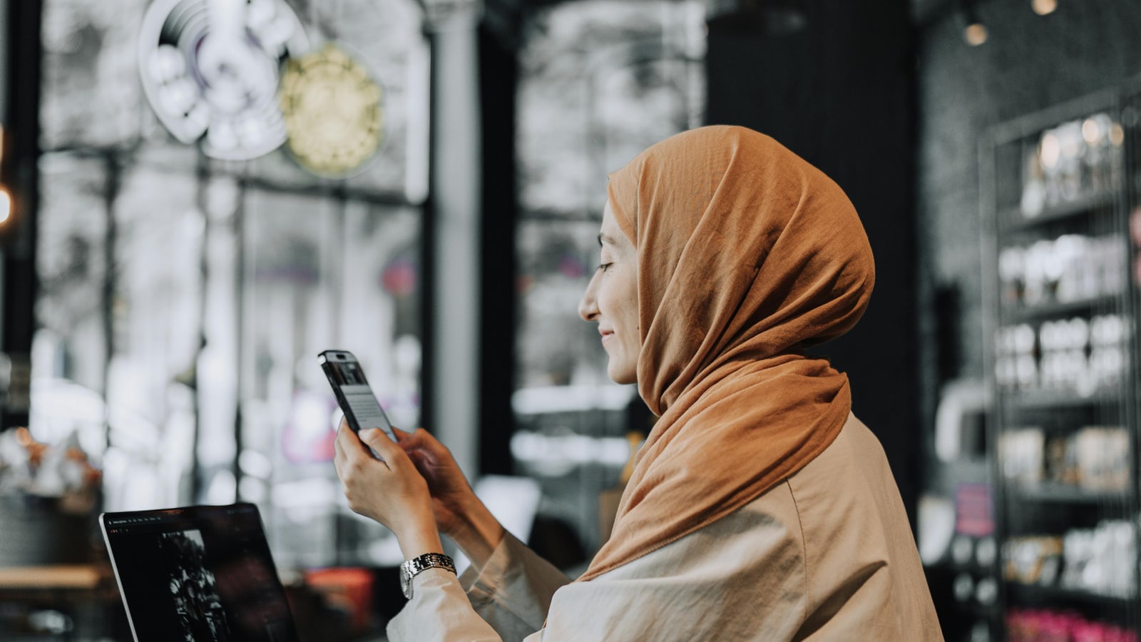 Pemilik bisnis meninjau laptop dan percakapan pelanggan di ponsel sebelum merapikan jalur jawaban dan handoff lead.